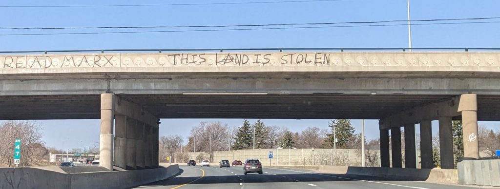 Overpass with "READ MARX" and "THIS LAND IS STOLEN" spray painted across it.